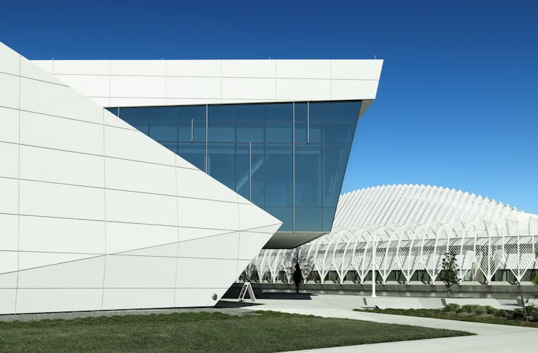 A large white, modern looking building is seen against a bright blue sky.